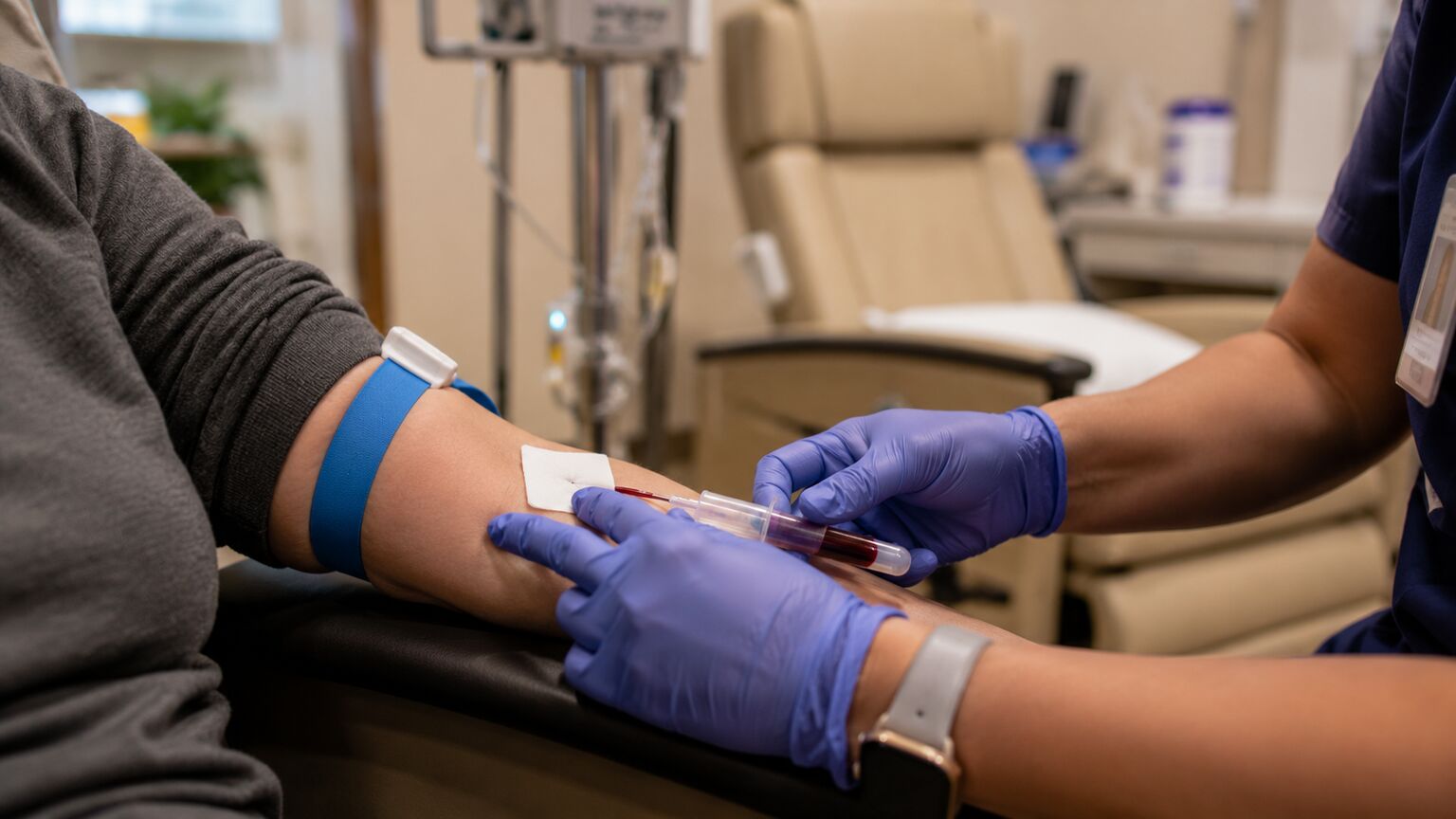Close-up of a phlebotomist drawing a baseline blood sample from a patient's arm before the start of chemotherapy infusion