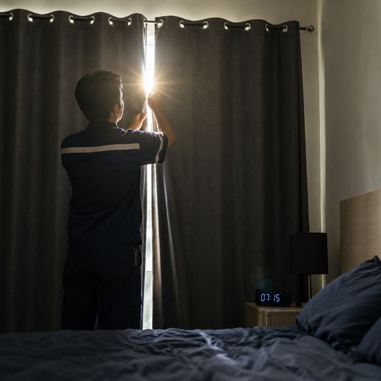 Close-up of a person in work clothes closing blackout curtains against bright daylight before sleeping